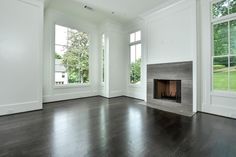 an empty living room with wood floors and white walls, fireplace in the middle between two large windows