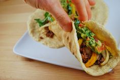 a person reaching for a taco on a plate with tortilla wrappers