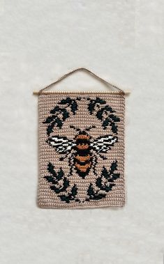 a small beaded wall hanging with a bee on it's back and leaves