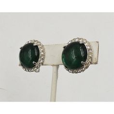 This is part of Chairish’s Costume Jewelry assortment.  Circa early 1950s round rhodium plated cabochon faux-emerald and clear round paste accents clip earrings. Marked "Castlecliff." Measure: 7/8 inches across. Condition: Very good; slight yellowing to a few rhinestones only noticeable upon very close inspection, minor wear to backs.  Please reference the measurements noted in the description above for the best approximate dimensions. Please reach out to the seller under "Ask the Seller" for sp Formal Silver Clip-on Earrings With 17 Jewels, Formal Round Clip-on Costume Earrings, Retro Round Clip-on Earrings For Formal Occasions, Classic Green Clip-on Earrings For Formal Occasions, Retro Round Clip-on Earrings For Party, Retro Round Clip-on Earrings For Evening, Vintage Round Clip-on Earrings For Party, Vintage Round Clip-on Earrings With Polished Finish, Vintage Sparkling Stones Clip-on Earrings For Evening