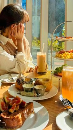 a woman sitting at a table with food and drinks in front of her on the phone