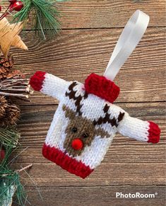 a knitted christmas ornament hanging on a wooden table next to pine cones