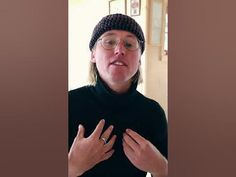 a woman wearing glasses and a beanie holds her hands together in front of her chest