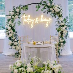 a table with white flowers and greenery under a neon sign that says today & baby's