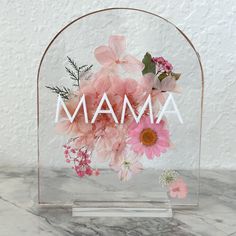 a clear acrylic sign with pink flowers and the word amam on it