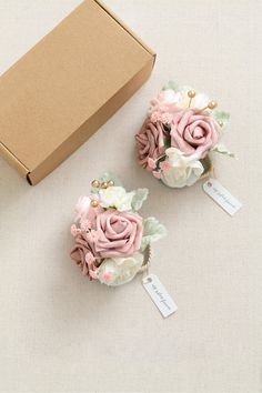 two small pink and white flowers sitting next to a brown box on a beige surface