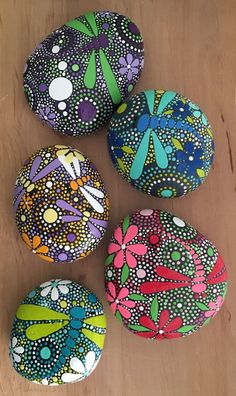 four painted rocks sitting on top of a wooden table next to each other, all decorated with flowers and dragonflies