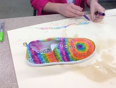 a woman sitting at a table with crochet shoes on it and colored markers in front of her