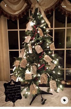 a decorated christmas tree in front of a window with cards attached to the top and bottom