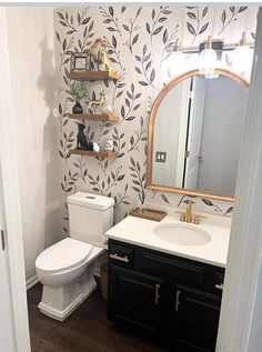 a white toilet sitting under a bathroom mirror next to a wooden sink vanity and black cabinets