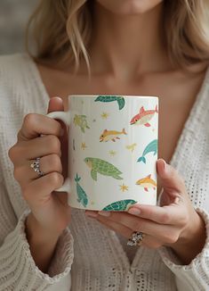 a woman is holding a coffee mug with fish on it