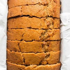 a loaf of banana bread sitting on top of a piece of white paper with some bananas in the background