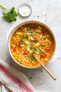 a pot filled with soup next to a wooden spoon and some parsley on the side