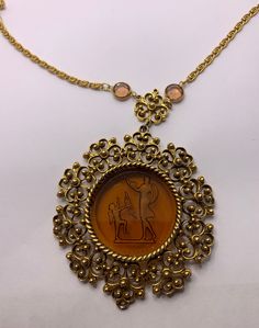 Vintage Goldette Cupid Venus necklace Gorgeous midcentury piece features a reverse carved glass cameo in  brown depicting Venus and Cupid  Gold tone chain and frame to cameo  round faceted rhinestones on chain  Unsigned. This particular piece has been attributed to Goldette and is consistent with that. There would have been a hang tag originally that I think is just missing now.  Spring ring clasp  In excellent vintage condition.Any wear such as an occasional small scratch its very minor. pendant is 2 1/2 inches in diameter entire pendant hangs at 3 1/2 inches long 22 inch long chain Venus And Cupid, Venus Necklace, Vintage Cupid, Cameo Necklace, Amber Color, Amber Glass, Long Chain, Hang Tags, Spring Rings