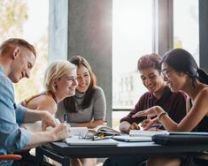 a group of people sitting around a table with notebooks and pens in their hands