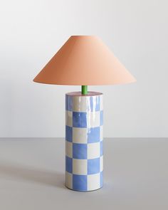 a blue and white checkered table lamp with a pink shade on the top, sitting on a grey surface