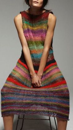 a woman is sitting on a chair wearing a multicolored knitted dress and heels