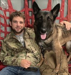 a man sitting in a red chair with his dog on the lap and wearing camo