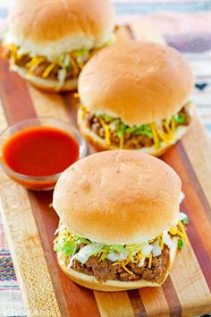 two sloppy joe sandwiches on a wooden cutting board with ketchup and mustard in the background