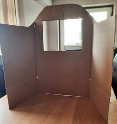 an open cardboard box sitting on top of a wooden table in front of a window