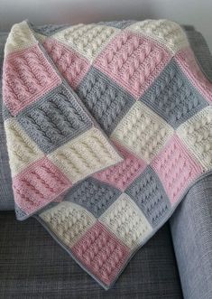 a crocheted blanket sitting on top of a gray couch next to a pillow