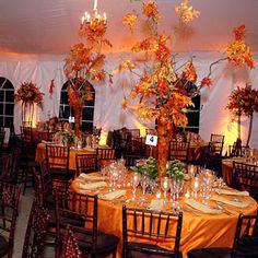 the tables are set up for an event with orange and yellow flowers in vases