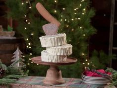 a three tiered cake sitting on top of a wooden plate next to a christmas tree