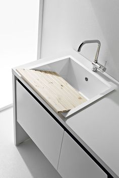 a sink with a cutting board on top of it in a room that has white walls and flooring