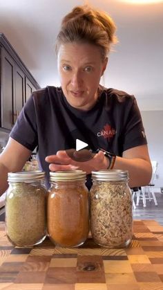 a woman standing in front of three jars filled with different types of spices and seasonings