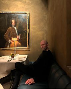 a man sitting at a table in front of a painting with a lamp on it