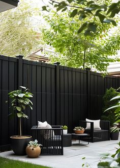 an outdoor living area with black furniture and plants on the side of the fenced in area