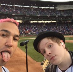 two young men with pink hair at a baseball game, one sticking out his tongue