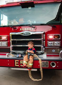 a young boy sitting on the front of a fire truck with his name written on it