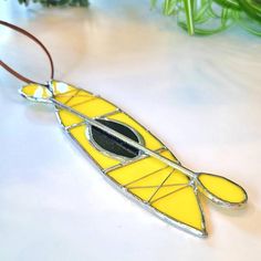 a yellow and black stained glass kayak ornament hanging from a leather cord