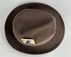 "You'll need this snazzy 1950's fedora to complete your look and turn your suit into an outfit! This fur felt fedora is chocolate brown with a cedar brown grosgrain ribbon band. It has a leather hat band and is fully lined. Made by \"Biltmore\" and sold by \"The Hat Guys\" in Oakland California. This hat is in great vintage condition with no holes, stains, or odors to note. Marked Size: 7 Inner circumference: 22\" Length (at longest point): 11.5\" Width (at widest point): 10.5\" Crown Height: 4\ Fitted Vintage Brown Fedora, Vintage Brown Felt Hat With Flat Bill, Vintage Brown Flat Bill Felt Hat, Vintage Fedora For Kentucky Derby With Flat Bill, Retro Brown Fedora Felt Hat, Vintage Fitted Felt Hat With Flat Bill, Retro Fitted Fedora With Curved Brim, Retro Fedora With Curved Brim, Retro Fitted Brimmed Fedora