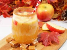 an apple cider is sitting on a cutting board next to some fall leaves and apples