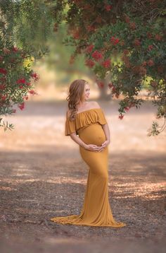 a pregnant woman in a mustard colored dress standing under a tree with red flowers on it