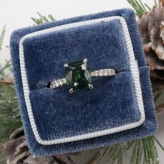 an engagement ring with a green emerald surrounded by white diamonds on a blue velvet box