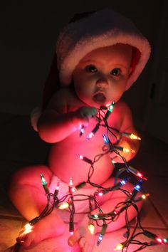 a baby is sitting on the floor with christmas lights