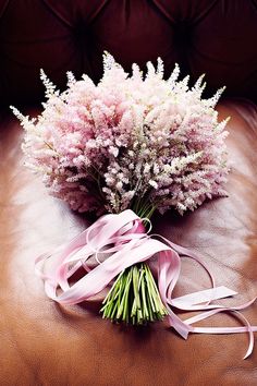 a bouquet of flowers sitting on top of a brown leather couch next to a pink ribbon