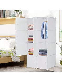 an open closet with clothes hanging on the door and folded towels in it, next to a bed