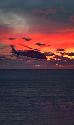 a helicopter flying over the ocean at sunset