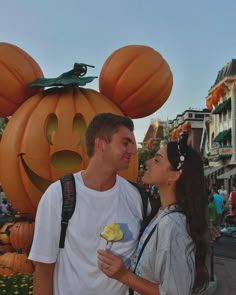 a man and woman standing next to each other in front of mickey mouse pumpkins