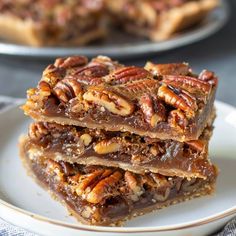 three pieces of pecan bar stacked on top of each other in front of another plate