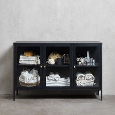 a black cabinet with towels and other items on the top shelf, in front of a white wall