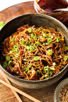 a bowl filled with noodles and green onions on top of a wooden table next to chopsticks