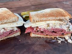 two sandwiches cut in half sitting on top of a cutting board next to pickles