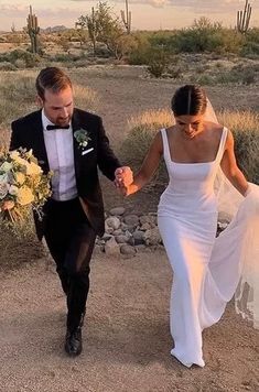 a bride and groom walking in the desert holding each other's hands as they hold hands