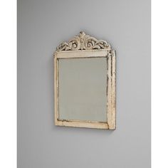 an old mirror hanging on the wall in front of a gray wall with a white frame