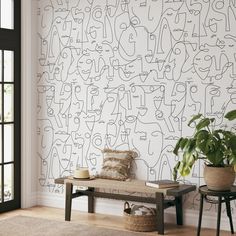 a room with a bench, plant and wallpaper on the walls that has faces drawn onto it